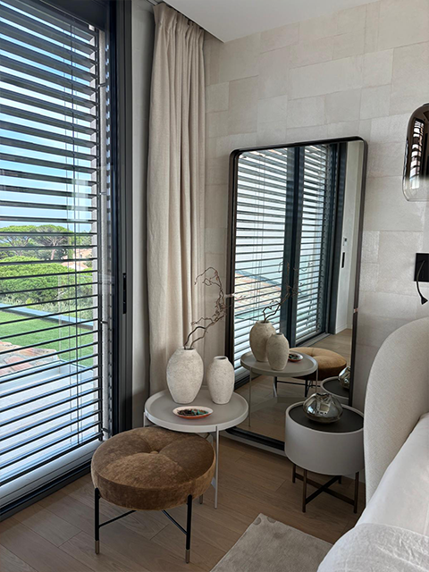 Coin détente près d’une baie vitrée avec miroir et tabouret.