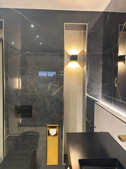 Salle de bain en marbre noir avec éclairage mural intégré.